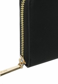 Sort pung lavet af tekstureret materiale med en guldfarvet lynlås. Har en kædetrækstangen med indgraveret brandingdetalje.