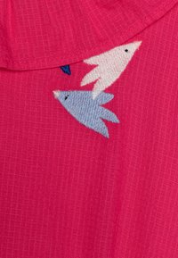 Kirkkaan vaaleanpunainen kangas, jossa on valkoisia ja vaaleansinisia kirjottuja lintuja. Pinta on sileä ja siinä on hienovarainen ruudullinen kuvio.