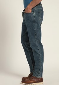 Jeans de mezclilla azul oscuro con un corte relajado, que cuentan con bolsillos, una cintura con cordón y un dobladillo vuelto. Zapatos de cuero marrón complementan el conjunto.