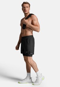 Zwarte sportshorts met een mesh binnenvoering, een elastische tailleband en reflecterende accenten, gecombineerd met witte sneakers met neon groene zolen.