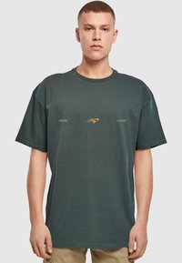 Mørkegrøn t-shirt lavet af bomuld, med rund halsudskæring, korte ærmer og et frontprint i guld med tekstelementer.