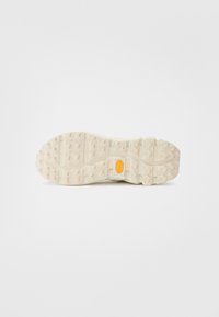 Semelle en caoutchouc beige clair avec une surface texturée, présentant un motif de grip distinctif et un logo Vibram orange visible.