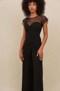 Black jumpsuit with sheer cap sleeves, fitted bodice, v-neckline, and wide-leg trousers featuring pleats; smooth texture.