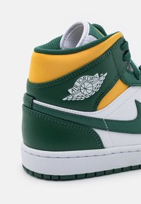 Talons de baskets Air Jordan verts, jaunes et blancs avec un logo représentant un ballon de basket et des ailes, coutures visibles et semelle texturée.