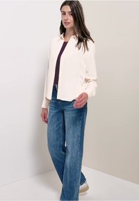 Crème knoop-overhemd met een relaxte pasvorm, gecombineerd met lichtblauwe wijde jeans. Bevat subtiele texturen en strakke lijnen.