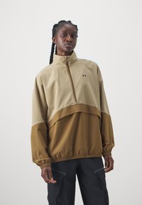 Beige ja pruun värvi poolzipiga pullover, millel on kerge kangas, kõrge krae ja elastsed mansetid. Omab Under Armour'i logo.