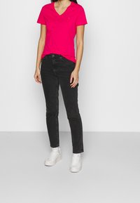 Camiseta fucsia de cuello en v con mangas cortas, combinada con jeans negros. El modelo lleva zapatillas blancas. Diseño simple, sin patrones ni acentos visibles.