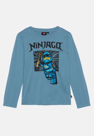 Niebieska koszula z długim rękawem z czarnym napisem "NINJAGO" oraz grafiką niebieskiego ninja LEGO trzymającego złotą broń w dynamicznej pozie.