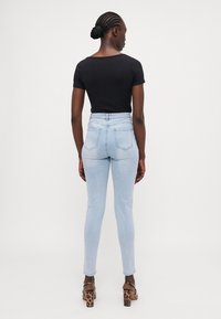 Jeans de tiro alto en un tono azul claro con corte ajustado, bolsillos traseros y una textura suave, combinados con una blusa negra de manga corta.