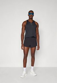 Svart atletisk tanktopp med en liten logo, kombinert med svarte shorts. Brukt med blå solbriller og hvite atletiske sko.