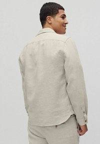Beige linnen shirt met lange mouwen, knoopsluiting bij de manchetten en een klassieke kraag. Subtiele textuur en een licht gebogen zoom aan de achterkant.