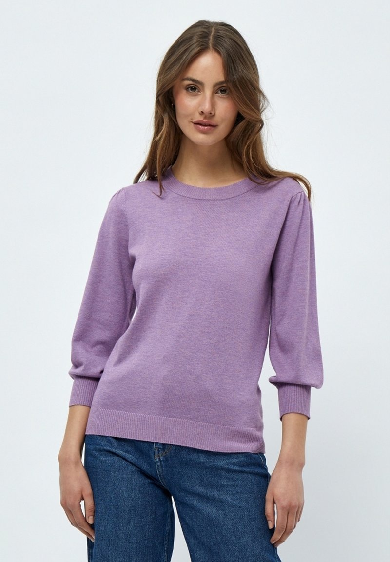 Lila Strickpullover mit Rundhalsausschnitt, 3/4 Puffärmeln sowie gerippten Bündchen und Saum. Kombiniert mit blauen Jeans.