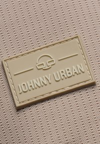 Barna gumi címke felnyomott "JOHNNY URBAN" felirattal és logóval, bélelt, textúrált világos bézs anyagra varrva.
