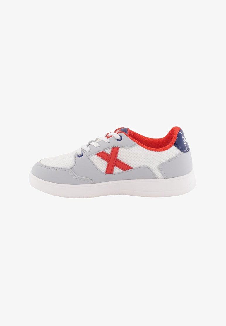 Zapatilla deportiva gris y blanca con parte superior de malla, acentuada por una "X" roja, suela de goma y forro rojo. Presenta un sistema de cordones tradicional.