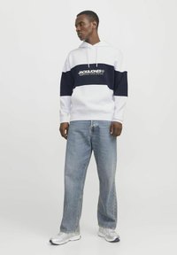 Hvid og navy stribet hoodie med central logo. Sammen med lyseblå vide jeans og sølvfarvede sneakers.
