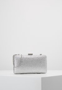 Pochette argentée avec une surface texturée ornée de petites décorations rondes. Comprend une bandoulière chaîne et une fermeture à fermoir métallique.
