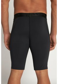 Shorts compressivi neri con vita elastica, texture liscia e design fino al ginocchio. Presentano cuciture visibili e logo sulla vita.