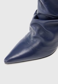 Botină din piele bleumarin, cu vârf ascuțit și un design cu partea superioară drapată, având o textură netedă și o construcție fără cusături.