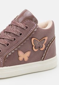 Paarse suède sneaker met vetersluiting, gegolfde details en roze en glitter vlinder appliqués. Witte rubberen zool met gestructureerde accenten.