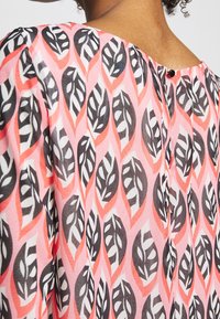 Blusa multicolore con un motivo fogliare rosa, nero e bianco, dotata di colletto tondo, pieghe e un piccolo bottone sul retro.