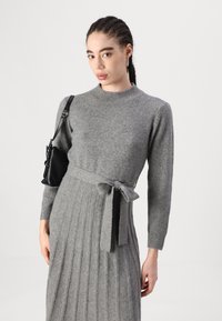 Hallide kudum Kleid, millel on sobiv kehaosa, soonikuline tekstuur ja vöödiga talje. Omab pikki varrukaid ja laiendatud seelikut vertikaalsete voldikutega.
