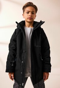 Giacca nera impermeabile con chiusura a zip, cappuccio regolabile e tasche laterali. Realizzata in tessuto resistente con finitura testurizzata.