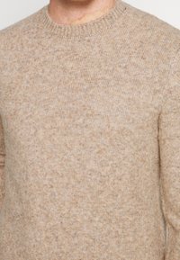 Maglione beige a maglia con scollo rotondo, motivo testurizzato e morbido tessuto in lana. Presenta un colletto a coste e maniche aderenti.