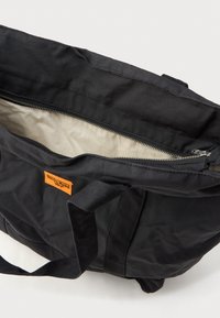 Μαύρη πάνινη τσάντα με διπλές λαβές, κλείσιμο με φερμουάρ και ανοιχτόχρωμο εσωτερικό. Διαθέτει πορτοκαλί ετικέτα με λογότυπο στο εξωτερικό.