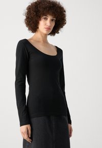 Top negro de manga larga con escote en forma de barco, hecho de una tela suave. El diseño es ceñido al cuerpo con una textura suave y un mínimo de detalles.
