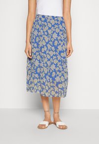 Gonna midi floreale blu, con motivi floreali chiari, vita elastica e tessuto leggero. Indossata con sandali bianchi flat.