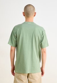 Light green cotton t-shirt with short sleeves and a relaxed fit, featuring a crew neckline and a smooth, slightly textured surface.