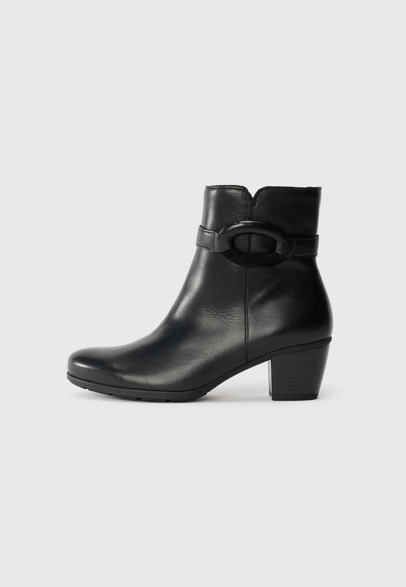 Bottine en cuir noir avec un bout arrondi, un talon moyen et une sangle décorative avec un détail de boucle circulaire. Texture lisse.