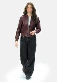 Burgunderfarbene Lederbomberjacke mit einem Frontreißverschluss, gerippten Bündchen und einer Seitentasche. Kombiniert mit lockeren schwarzen Jeans und schwarzen Schuhen.