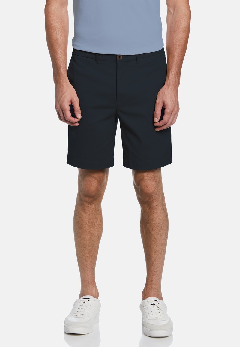 Marineblaues Shorts aus strapazierfähigem Stoff, mit flachem Vorderdesign, Knopfverschluss und Seitentaschen. Getragen mit weißen Sneakern.