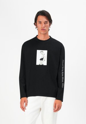 Schwarzes langärmliges T-Shirt mit einem weißen fotographischen Druck auf der Vorderseite und Text entlang des Ärmels. Baumwollmaterial mit lockerer Passform.