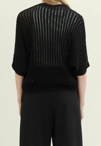 Zwart gebreid top met een losse, open geweven structuur, korte mouwen en een geribde zoom. De textuur is ademend, ideaal om in laagjes te dragen.