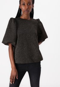Textuurrijke zwarte top met pofmouwen, voorzien van een geometrisch patroon en een ronde halslijn, gecombineerd met donkere, slim-fit jeans.