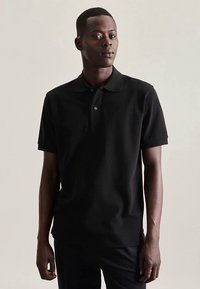 Zwart poloshirt van katoenmix met korte mouwen, dries knoopsluiting en subtiel logodetail op de borst. Soepele textuur.