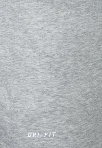 Tela Dri-FIT gris con un aspecto texturizado; presenta la inscripción "DRI-FIT" en blanco en la parte inferior. Material suave y ligero.