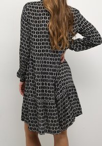 Abito bianco e nero con un motivo geometrico esagonale, maniche lunghe e una gonna a strati che si allarga dalla vita.