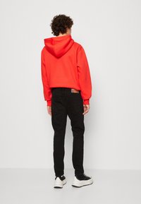 Punainen huppari, jossa edessä kengurutasku, yhdistetty mustiin farkkuihin ja mustiin lenkkareihin. Kangas näyttää sileältä ja istuvuus on rento.