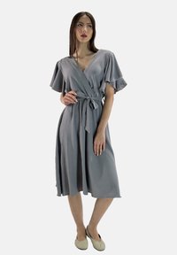 Robe enveloppante grise avec des manches flottantes, une taille nouée et une silhouette fluide, fabriquée en tissu léger avec une finition texturée.