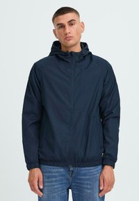 Navy lightweight jacket with a hood, zipper closure, elastic cuffs, and a drawstring hem. Features side pockets and a smooth texture.