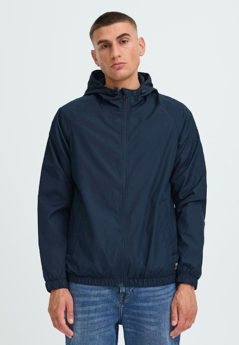 Navy lightweight jacket with a hood, zipper closure, elastic cuffs, and a drawstring hem. Features side pockets and a smooth texture.