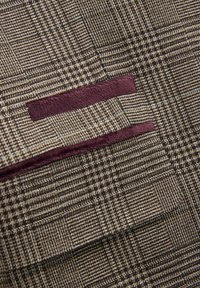 Strukturiertes Gewebe in Braun und Beige mit einem karierten Muster, das burgunderfarbene Details und sichtbare Nähte entlang der Kanten aufweist.