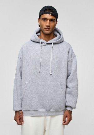 Lichtgrijze hoodie met een voorzak, losse pasvorm en koordjes. Heeft geribbelde manchetten en zoom, gemaakt van zachte stof.