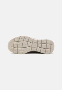 Light beige sneaker outsole, textured rubber with a grid pattern, featuring raised sections and grooves for grip.