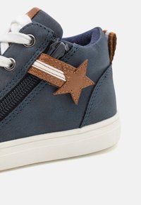 Sneakerki w kolorze niebieskim, wykonane z syntetycznego materiału, z brązowym skórzanym akcentem w kształcie gwiazdy, białymi paskami, zamkiem błyskawicznym po bokach oraz białą gumową podeszwą.