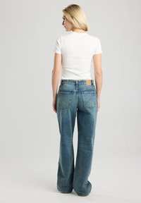 Jeans in denim blu con una vestibilità comoda, caratterizzati da una vita alta, tasche posteriori e un lavaggio chiaro. Abbinati a una maglietta bianca a maniche corte.