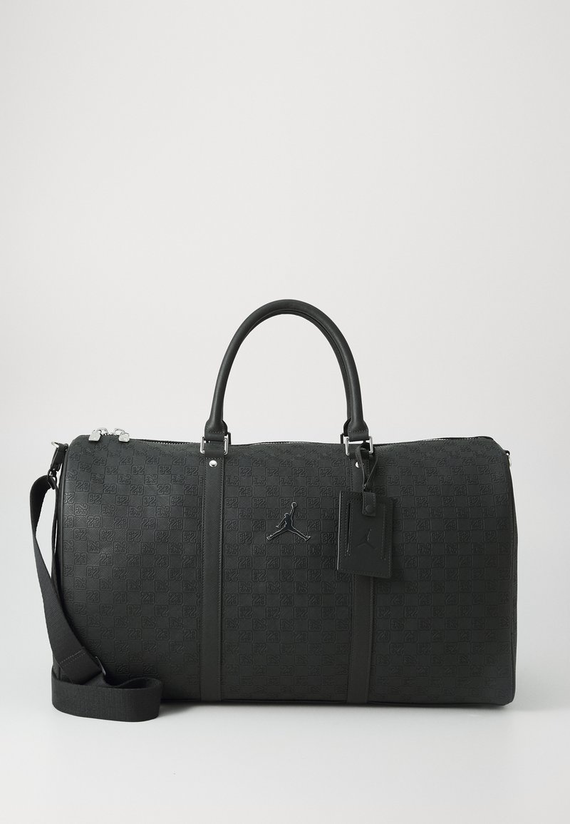 Geantă de duffel neagră cu un model texturat, având un logo, două mânere, curea de umăr detașabilă și fermoar din metal argintiu.